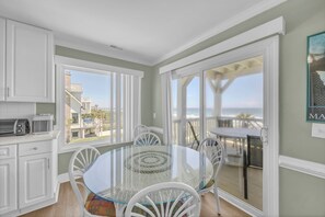 A dining area with a glass table and chairs, a kitchen with white cabinets, and a view of the ocean through large windows.