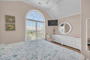 A bedroom with a large bed, a dresser, a TV, a window with blinds, and wall art. - Maultsby -Enjoy amazing ocean front views from this 10 bedroom home (Wrightsville Beach)