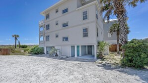 A multi-story beachfront building with a sandy driveway, palm trees, and a wooden fence. - Maultsby -Enjoy amazing ocean front views from this 10 bedroom home (Wrightsville Beach)