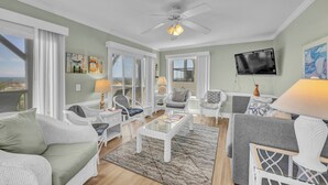 A spacious living room with white wicker furniture, a glass coffee table, and a ceiling fan. - Maultsby -Enjoy amazing ocean front views from this 10 bedroom home (Wrightsville Beach)
