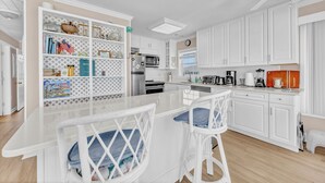 A kitchen with white cabinets, a central island, bar stools, and a built-in bookshelf. - Maultsby -Enjoy amazing ocean front views from this 10 bedroom home (Wrightsville Beach)