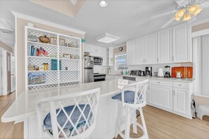 A kitchen with white cabinets, a central island, bar stools, and a built-in bookshelf. - Maultsby -Enjoy amazing ocean front views from this 10 bedroom home (Wrightsville Beach)