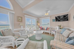 A spacious room with white wicker furniture, a round table, and a large TV on the wall.