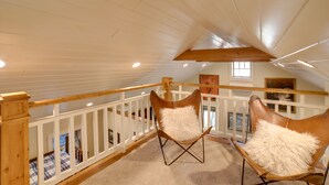 A loft bedroom with a high ceiling, wooden beams, a white railing, and two leather chairs with fluffy pillows. - Pool Access: Pet-Friendly Pennsylvania Cabin! (Laughlintown)