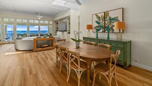 A spacious living area with a wooden dining table, wicker chairs, a sofa, and a view of the ocean through large windows. - Hale Ilikai By Parrish Kauai: fabulous family location with oceanfront views and (Koloa)