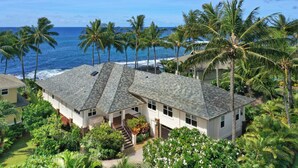 A coastal house with a stone roof, surrounded by lush greenery and palm trees, overlooking the ocean. - Hale Ilikai By Parrish Kauai: fabulous family location with oceanfront views and (Koloa)