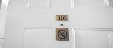 A white door with a number plate reading "110" and a no-smoking sign.