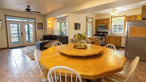 Un vaste espace de vie comprenant une table à manger en bois, des chaises blanches et un ventilateur de plafond.