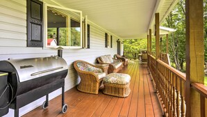 Une véranda couverte avec un barbecue, des meubles en osier et une rambarde en bois.