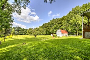 Une maison blanche avec un toit rouge, entourée de champs verdoyants et d’arbres.