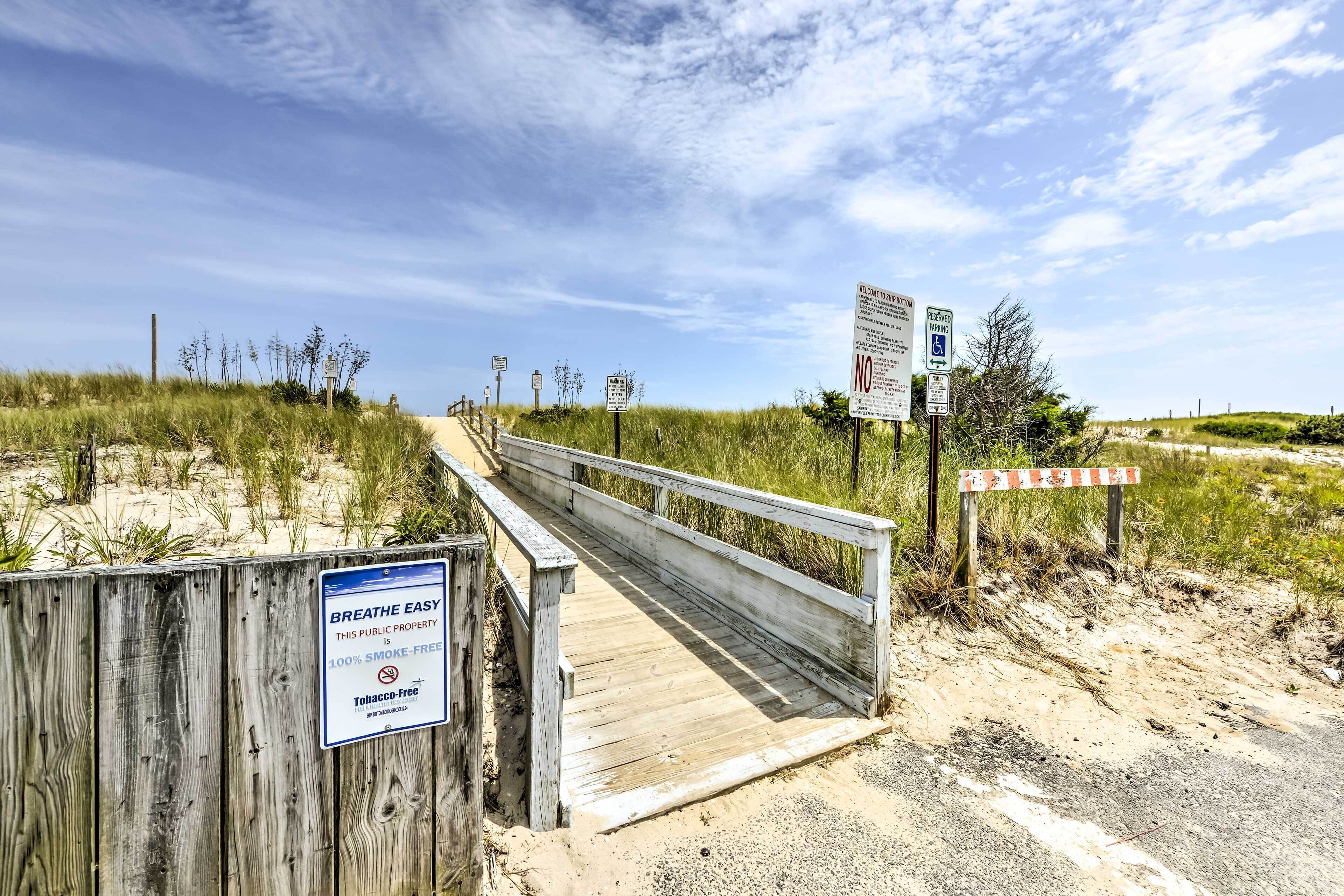 A wooden boardwalk leading to a beach area with signs indicating smoking restrictions and parking information.