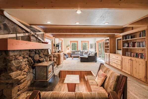 A cozy living room with a stone fireplace, wooden furniture, and a bookshelf.