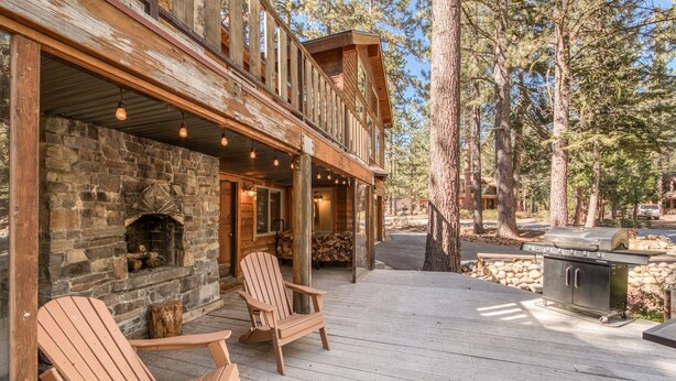 Une terrasse en bois avec des fauteuils Adirondack, une cheminée en pierre et un espace barbecue.