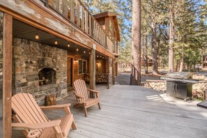 A wooden deck with Adirondack chairs, a stone fireplace, and a grill area.