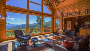 A log cabin interior with large windows, a fireplace, and a cozy seating area. - At Last Lodge | Pet Friendly Log Cabin with Hot Tub, Grill + VIEWS! (Old Fort)