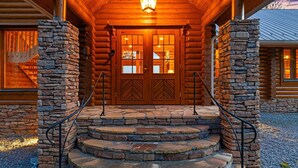 A log cabin with a stone staircase leading to a wooden door with glass panels. - At Last Lodge | Pet Friendly Log Cabin with Hot Tub, Grill + VIEWS! (Old Fort)