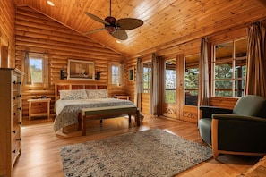 Une chambre dans un chalet en rondins, avec un lit, une chaise, une table de chevet, une commode et un ventilateur de plafond.