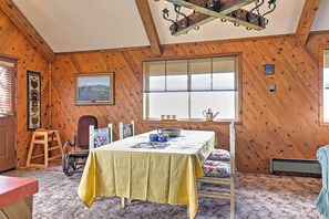 A room with wooden walls and a table set with a yellow tablecloth. There is a window with blinds, a chair, and a ladder. - Hideaway on Working Cattle Ranch 26 Mi to Rogerson (Rogerson)
