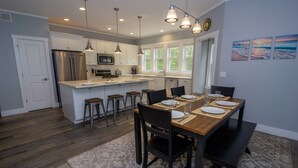A modern kitchen with a central island, bar stools, and a dining table set for four. - 5 Bedroom Beachwalk Resort w/ Golf Cart & Pool Access (Michigan City)
