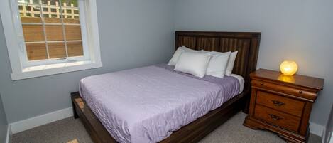 Un dormitorio con una cama de madera, una mesita de noche con una lámpara y una ventana que da a una valla de madera.