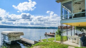 Ein Anwesen am Seeufer mit überdachter Anlegestelle, Außenbereich mit Sitzgelegenheiten und einem gläsernen Gebäude mit Seeblick.