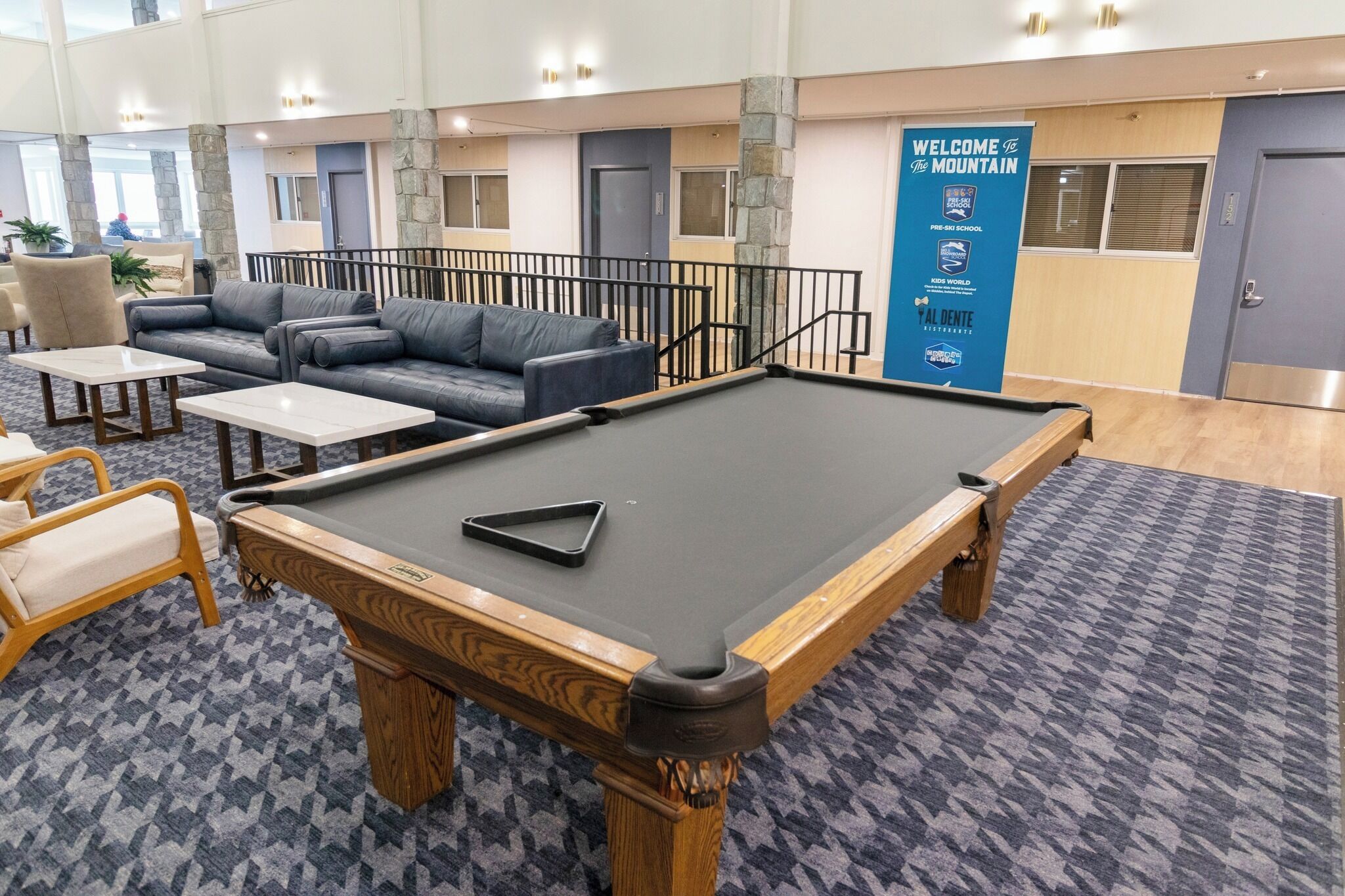 Une table de billard dans un hall d’entrée, avec un canapé et des fauteuils, un panneau d’accueil et un pilier en pierre.
