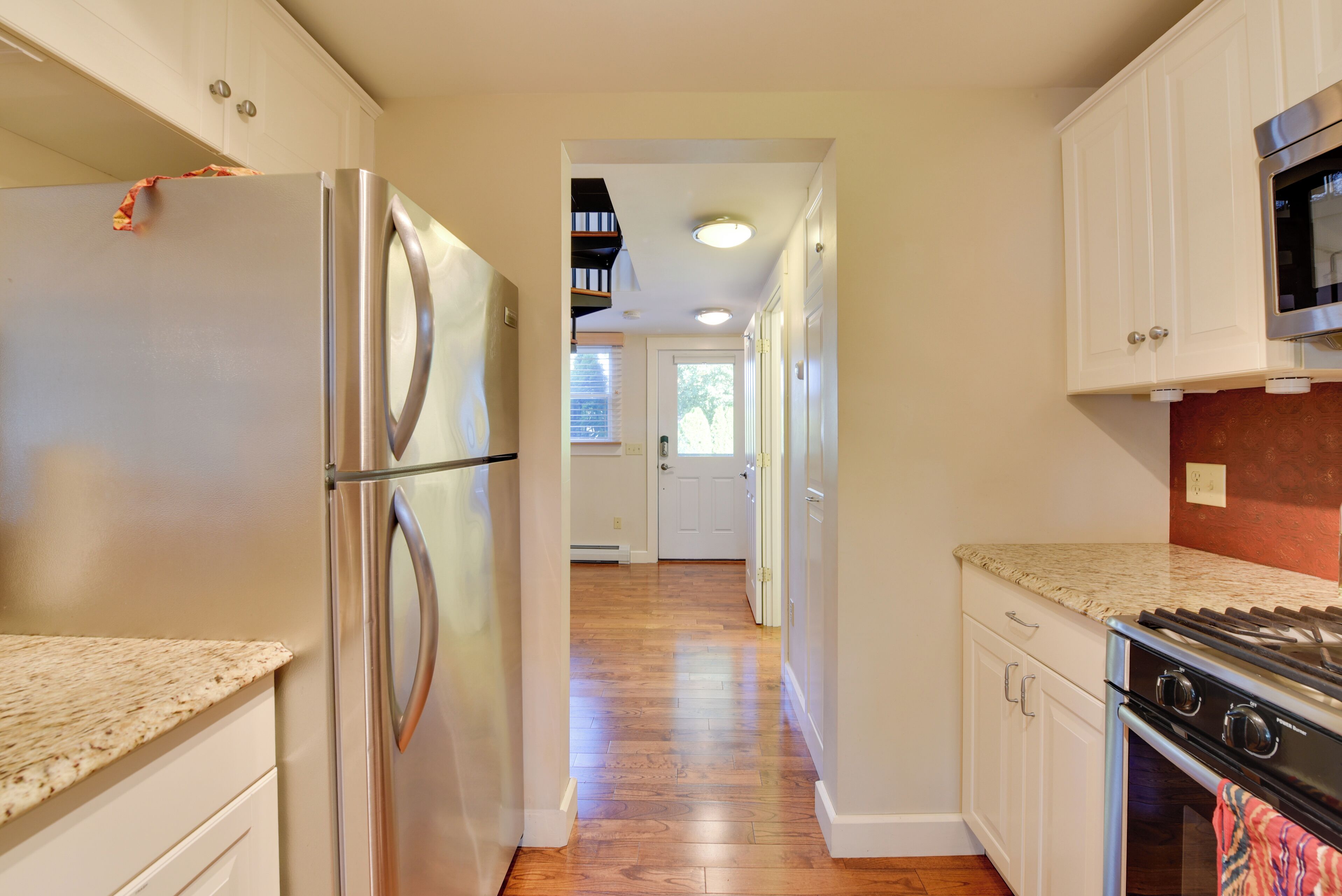 A kitchen with a stainless steel refrigerator, wooden flooring, white cabinets, and a granite countertop.