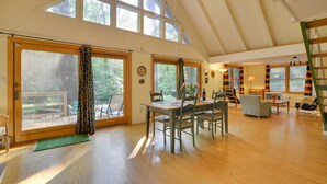 Una habitación amplia con techo alto, ventanas grandes, una mesa de comedor de madera con sillas, un sofá y una escalera.