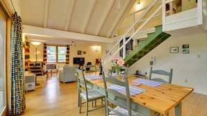 Amplia sala de estar con una mesa de comedor de madera, sillas verdes, una escalera y vistas al exterior.