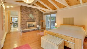 Un dormitorio espacioso con techo de madera, chimenea de ladrillo y una cama grande.