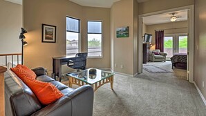 A spacious living room with a leather sofa, a glass coffee table, and a desk with a chair. There are two windows providing natural light, a ceiling fan, and a view of the outdoors. - Golf Course View & Pool Access: Gold Canyon Gem (Gold Canyon)