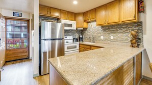 A kitchen with wooden cabinets, a stainless steel refrigerator, a microwave, and a stone backsplash. - Pristine Lihue Condo w/ Balcony: Walk to Beach! (Lihue)
