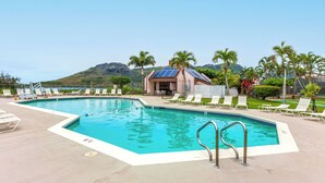 A swimming pool with lounge chairs, a small building with solar panels, and a mountain in the background. - Pristine Lihue Condo w/ Balcony: Walk to Beach! (Lihue)