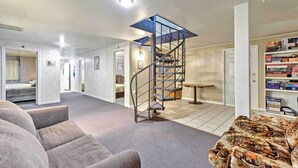 A modern living room with a spiral staircase, a sofa, a patterned armchair, and a bookshelf. - Huge Preston Cabin w/ Game Room & Mountain Views! (Preston)
