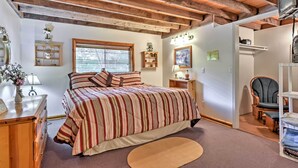 A bedroom with a wooden ceiling, a bed with striped bedding, a nightstand, a lamp, a chair, and a television. - Huge Preston Cabin w/ Game Room & Mountain Views! (Preston)