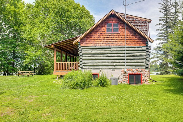 A log cabin with a wooden porch, a stone foundation, and a red door.
