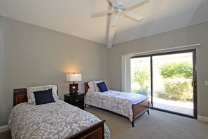 A bedroom with two beds, a ceiling fan, a nightstand with a lamp, and a sliding glass door leading to a balcony.