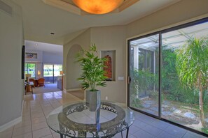A spacious interior with a glass door leading to a garden, a round table with a plant, and a dining area in the background.