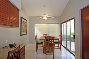 A dining area with a table and chairs, a ceiling fan, a window with a view, and a door. - Golf course-view 2BR condo in PGA West with pool, patio, and fireplace. (La Quinta)