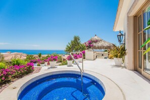Ein Pool mit Blick auf den Ozean, umgeben von Kübelpflanzen und einem Gebäude mit einem Reetdach.