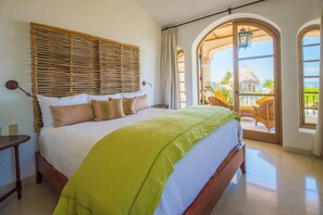 Ein Schlafzimmer mit einem großen Bett, einem Holz-Kopfteil und Blick auf ein Gebäude mit Strohdach.