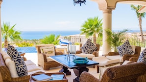 A sunlit outdoor seating area with wicker furniture, a table, and a view of the ocean. - Luxury Cabo del Sol Villa w/ Cook, Infinity Pool, Hot Tub, Firepit, & Golf Views (Turistico Corredor)