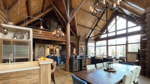A spacious log cabin interior with a large dining table, wooden cabinets, and a kitchen area. - ALPEN RIDGE- Elevated Luxury Estate with Slopeside Views and Access (Mountain Village)