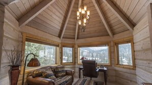 Un interior acogedor de cabaña de madera con un sofá de cuero, un reposapiés estampado, un escritorio y una araña.