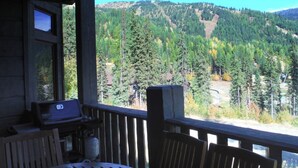 Una terraza de madera con mesa y sillas, con vistas a un paisaje montañoso y boscoso.