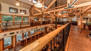 A spacious multi-level interior with wooden beams, multiple seating areas, and large windows offering views of the outdoors.