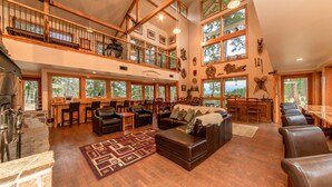 A spacious interior with a high ceiling, wooden beams, a fireplace, a dining area, and a seating area with leather furniture.
