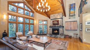 A spacious living room with a fireplace, large windows, and a high ceiling.
