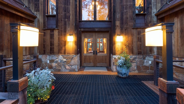 A wooden building entrance with a stone wall, a large door, and two potted plants.