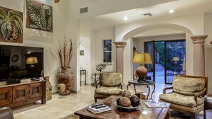 A spacious living room with a wooden coffee table, two armchairs, a TV, and decorative vases.